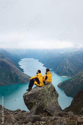 Obraz na plátně hikers couple sitting on the top of mountain near blue norway lake