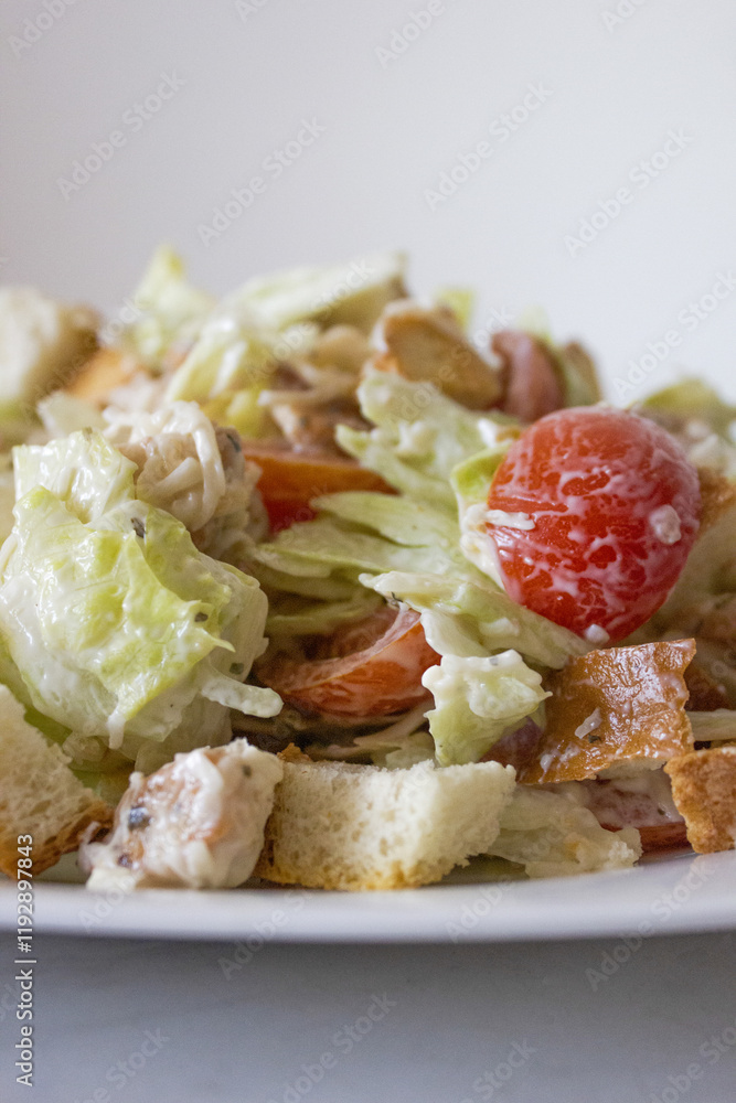 Fresh Caesar salad with lettuce, cherry tomatoes, croutons, chicken, and creamy dressing on a white plate creates a vibrant and appetizing look