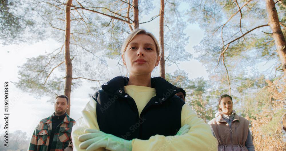 Obraz premium Serious woman looking at camera after collecting plastic. Cleaning up nature from plastic waste. Bags with trash located on ground. Woman crossing her hands.
