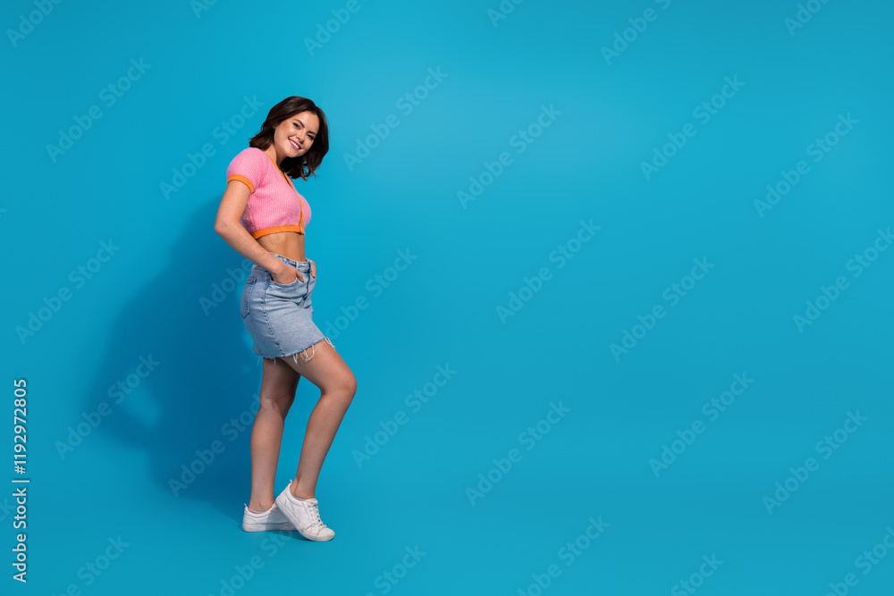Trendy young woman wearing casual stylish outfit on blue background, smiling confidently, standing in relaxed pose Trendy young woman wearing casual stylish outfit on blue background, smiling confidently, standing in relaxed pose