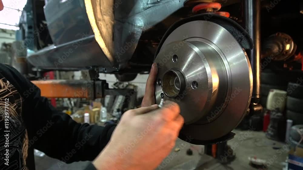Young mechanic repairs and restores an old gray car after a road accident, repairing the rear suspension and installing new brake discs Young mechanic repairs and restores an old gray car after a road accident, repairing the rear suspension and installing new brake discs