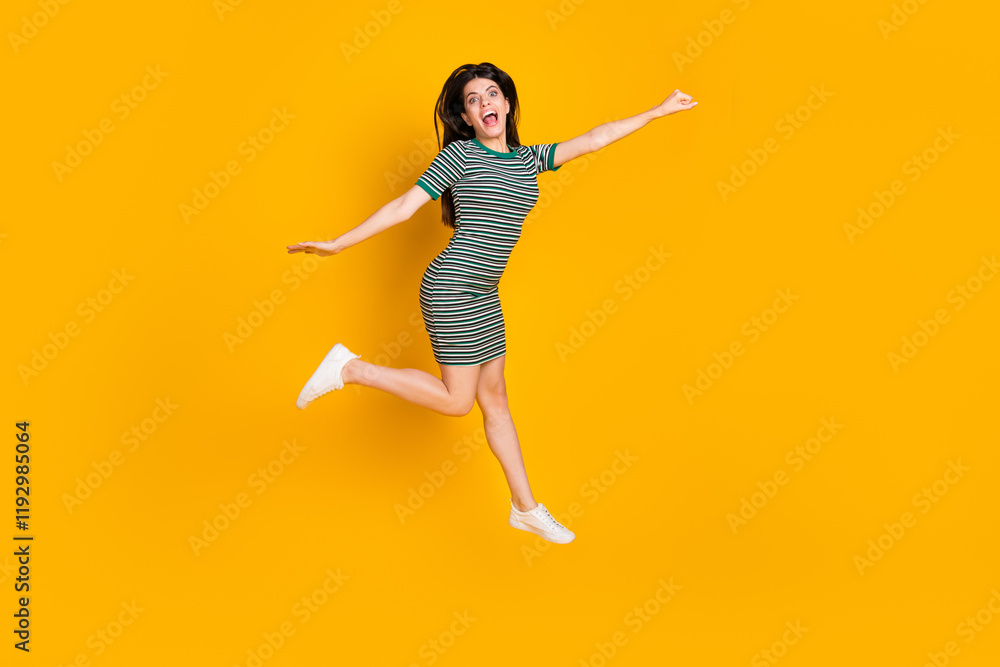Cheerful young woman in a striped dress joyfully jumping on a vibrant yellow background expressing happiness and positive energy Cheerful young woman in a striped dress joyfully jumping on a vibrant yellow background expressing happiness and positive energy