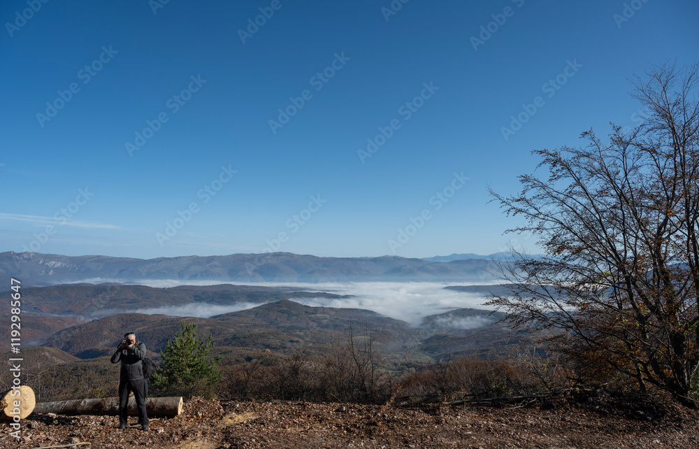 Obraz premium A nature photographer takes a photo of a mountain range that is partially covered in fog, with a beautiful clear blue sky above. A beautiful nature photo.