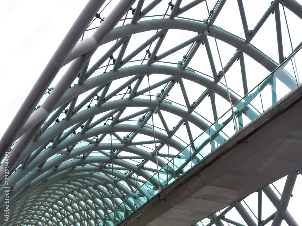 Scene of modern construction of arch ceiling over the glass pathway, bridge of peace, Tbilisi architecture in Georgia. Curved structure supporting roof in building, curvature line background. Scene of modern construction of arch ceiling over the glass pathway, bridge of peace, Tbilisi architecture in Georgia. Curved structure supporting roof in building, curvature line background.