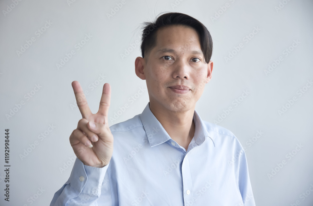 Healthy happy smiling middle aged southeast asian man pointing 2 fingers up, v for victory gesture, concept of two points, number two, second place on isolated background Healthy happy smiling middle aged southeast asian man pointing 2 fingers up, v for victory gesture, concept of two points, number two, second place on isolated background