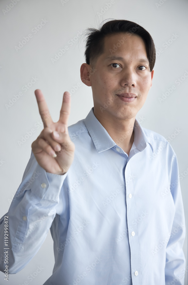 Healthy happy smiling middle aged southeast asian man pointing 2 fingers up, v for victory gesture, concept of two points, number two, second place on isolated background Healthy happy smiling middle aged southeast asian man pointing 2 fingers up, v for victory gesture, concept of two points, number two, second place on isolated background