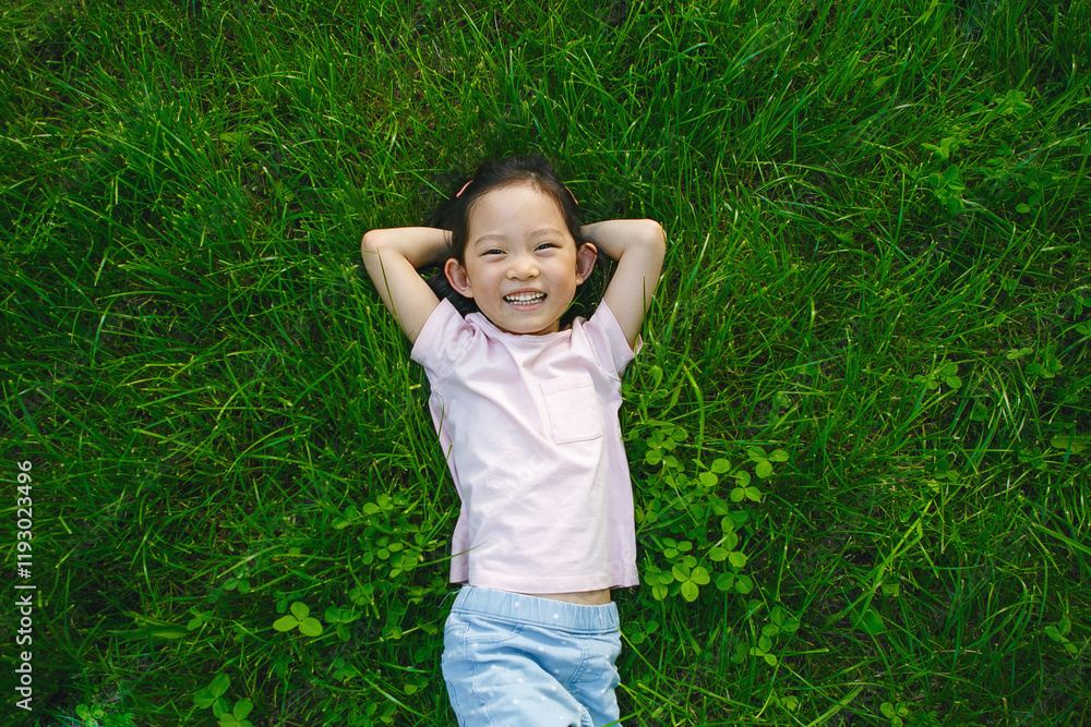 Smiling Little Girl Lying On Grass In Park On Sunny Day And Look to Camera, Overhead View Smiling Little Girl Lying On Grass In Park On Sunny Day And Look to Camera, Overhead View