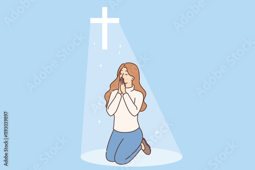 Christian woman prays on knees under religious crucifix or cross emitting bright light