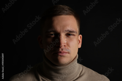 Distressed young man crying on black background