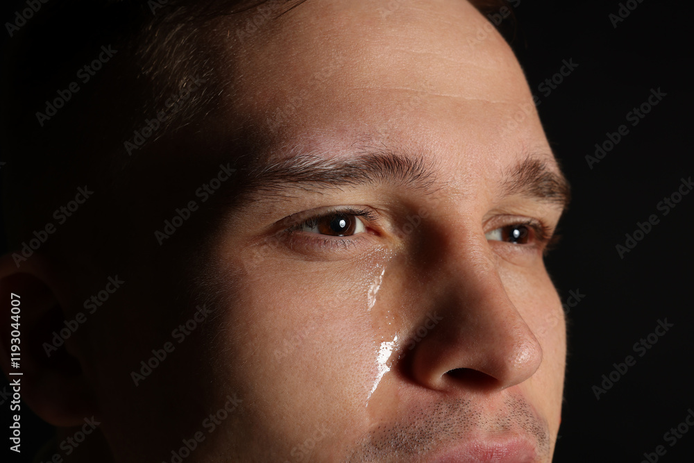 Distressed young man crying on black background, closeup Distressed young man crying on black background, closeup