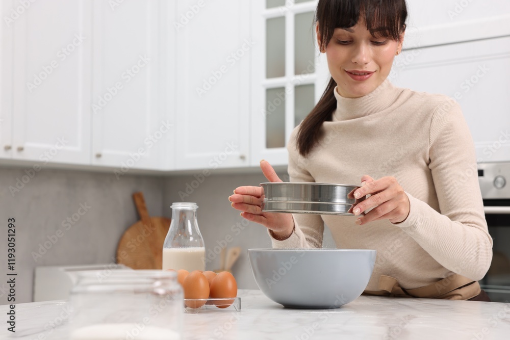 Making dough. Woman sifting flour into bowl at white table. Space for text Making dough. Woman sifting flour into bowl at white table. Space for text