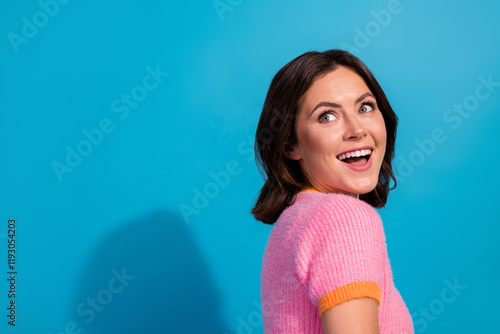 Cheerful young brunette woman showing happiness with a charming smile, standing against a vivid blue backdrop photo