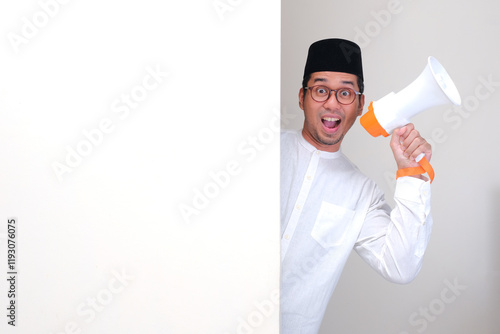 A muslim man peeking behind wall holding megaphone with wow face expression photo