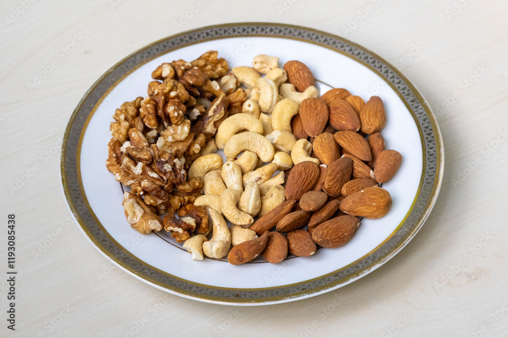 Three kinds of nuts – walnuts, cashews, and almonds – served in a white ceramic plate on a light wooden background. Three kinds of nuts – walnuts, cashews, and almonds – served in a white ceramic plate on a light wooden background.