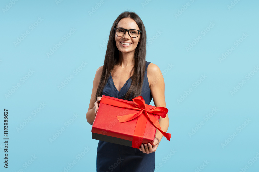 Happy Hispanic woman holding red gift box with ribbon isolated on blue background Happy Hispanic woman holding red gift box with ribbon isolated on blue background