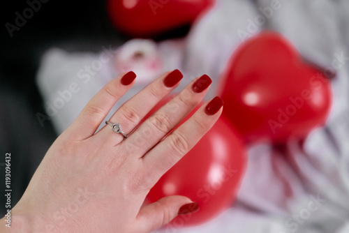 A woman's hand with a ring on her middle finger, her beloved proposed, surrounded by beautifully decorated heart-shaped balloons. photo