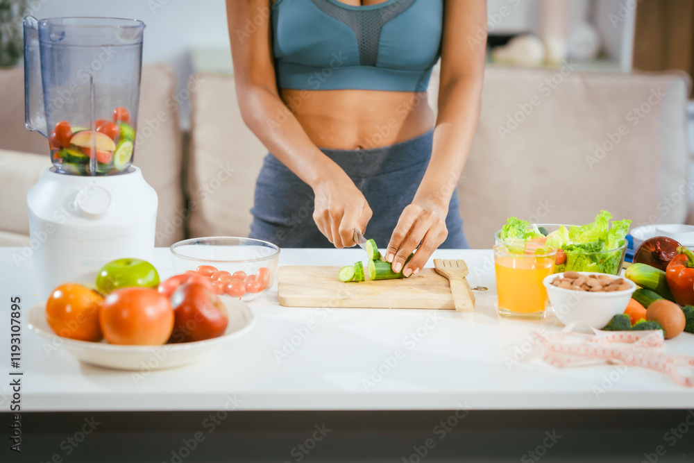 An African American woman in sportswear sits on a sofa near the dining table, preparing a healthy salad with vegetables fruits, drinking juice after exercise for weight control and low-fat nutrition An African American woman in sportswear sits on a sofa near the dining table, preparing a healthy salad with vegetables fruits, drinking juice after exercise for weight control and low-fat nutrition