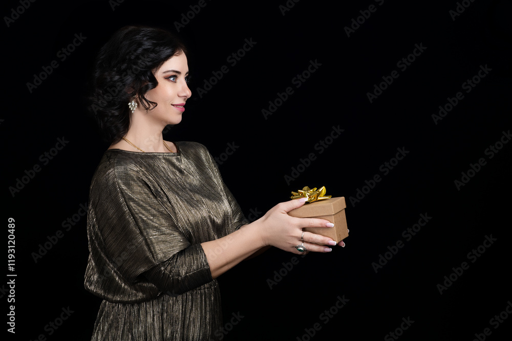 Fashion beautiful woman in a golden shiny dress smiling on a black background with a gift box in her hand happy with black hair and blue eyes Fashion beautiful woman in a golden shiny dress smiling on a black background with a gift box in her hand happy with black hair and blue eyes