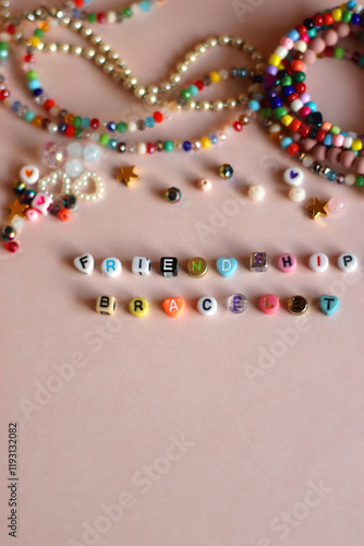 Friendship bracelet spelled with letter beads. Colorful handmade bracelets and various beads. Top view, pink background.
