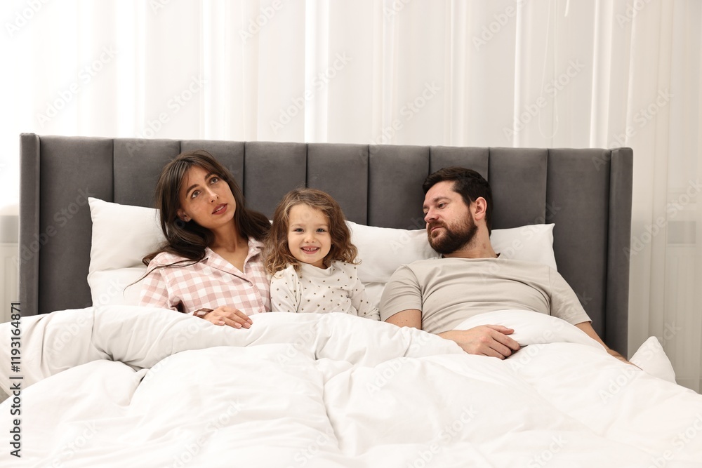 Fototapeta premium Happy playful daughter with her overwhelmed parents in bed at home