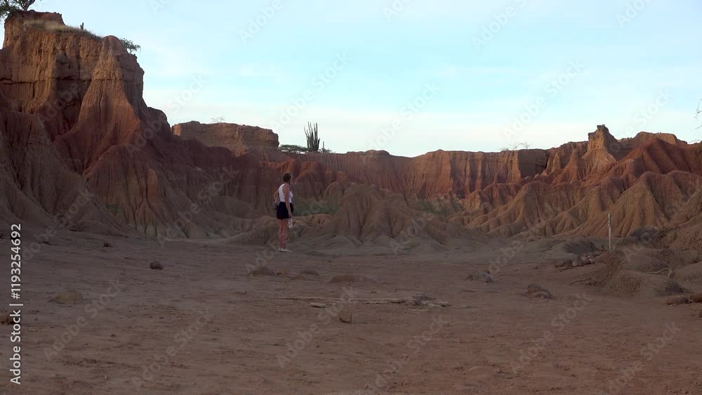 A wide shot of a woman looking at dry rock formations in the Tatacoa Red Desert during sunset A wide shot of a woman looking at dry rock formations in the Tatacoa Red Desert during sunset