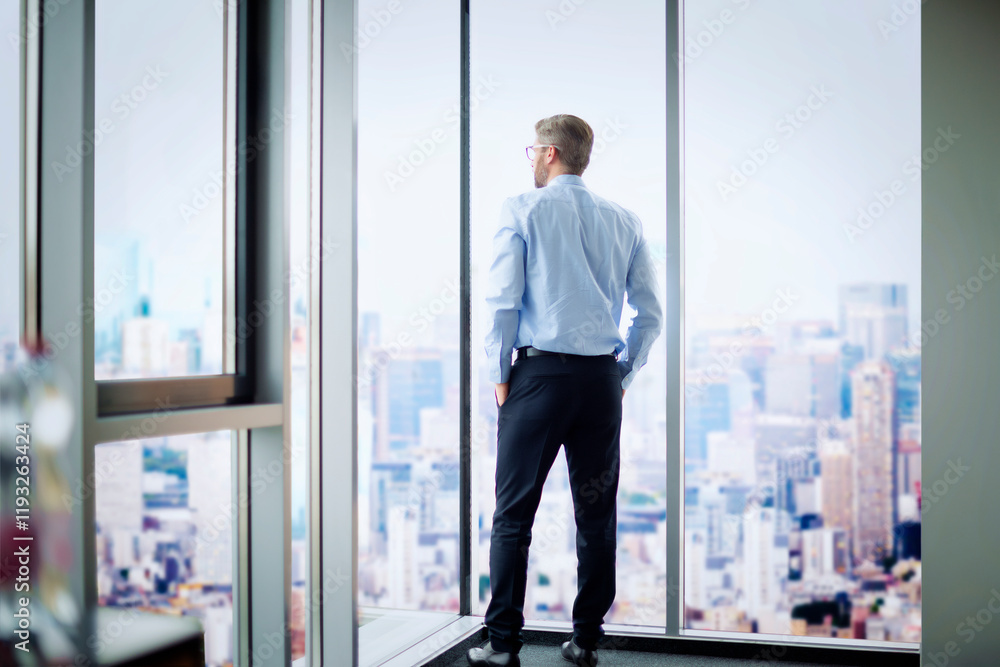 Rear view of a businessman standing in a modern office and looking out of over the city Rear view of a businessman standing in a modern office and looking out of over the city