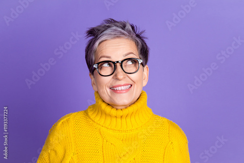 Fotografie Cheerful mature woman in yellow sweater with glasses looking up against purple b