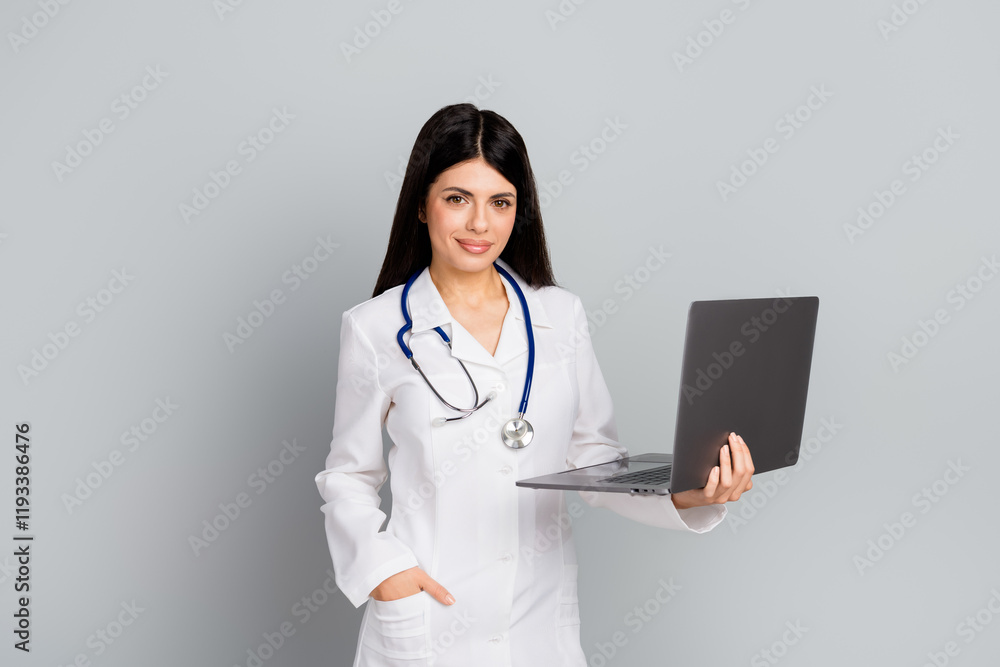 Female doctor with stethoscope holding laptop on grey background Female doctor with stethoscope holding laptop on grey background