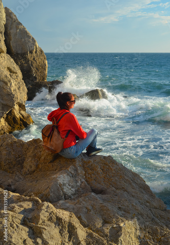 Obraz na płótnie Happy female tourist with a backpack on the top of a mountain, enjoying the sea view, standing on a rock and looking into the distance. The village of Novy Svet in Crimea. Russia w salonie