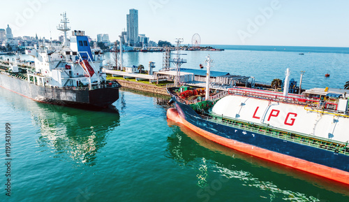 LPG tanker and cargo ship near industrial port with urban skyline in background, captured from elevated angle. Reflection on water highlights maritime trade and energy logistics.