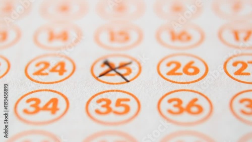 A man marks with a pen numbers 25, 46, 44, 67, 75 on a lottery ticket. The rows of orange numbers in orange circumferences on the white ticket are arranged horizontally. Close-up horizontal video photo