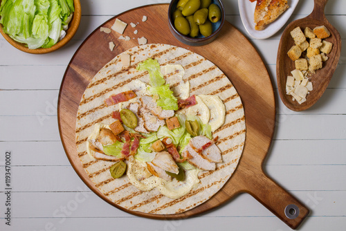 Chicken bacon caeser wrap ingredients on round wooden serving board. Chicken breast fillets wraps. View from above, top view photo