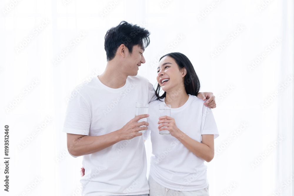 Asian couple enjoying drinking water and sharing smiles against white curtain background Asian couple enjoying drinking water and sharing smiles against white curtain background