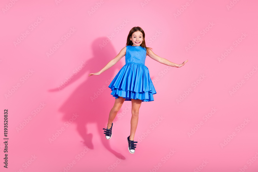 Adorable young girl in a blue dress jumping against a pink background Adorable young girl in a blue dress jumping against a pink background