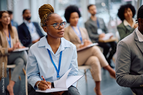 Young black businesswoman taking notes while attending education event in board room. photo