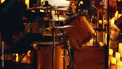Close-up of a drum kit being played on a dimly lit stage surrounded by candles.