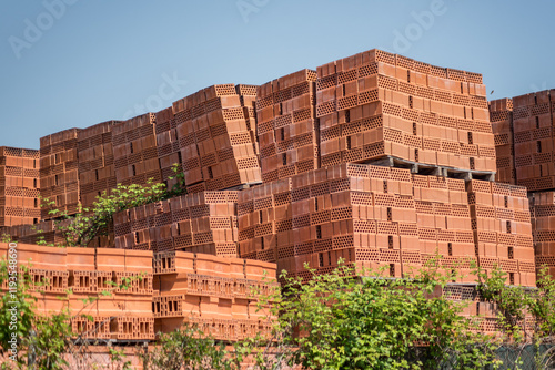 Una gran cantidad de ladrillos de terracota están apilados sobre palés al aire libre. Los ladrillos son de un cálido color marrón rojizo y están ordenados cuidadosamente.  photo