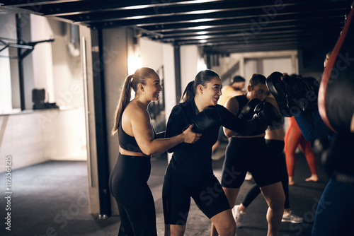 Smiling female coach helping a young woman wearing boxing gloves doing a punching workout during a boxing class in a gym photo