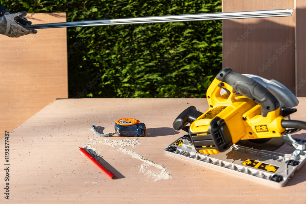 Obraz premium Male using electric circular saw to cut DIY sheet material outside