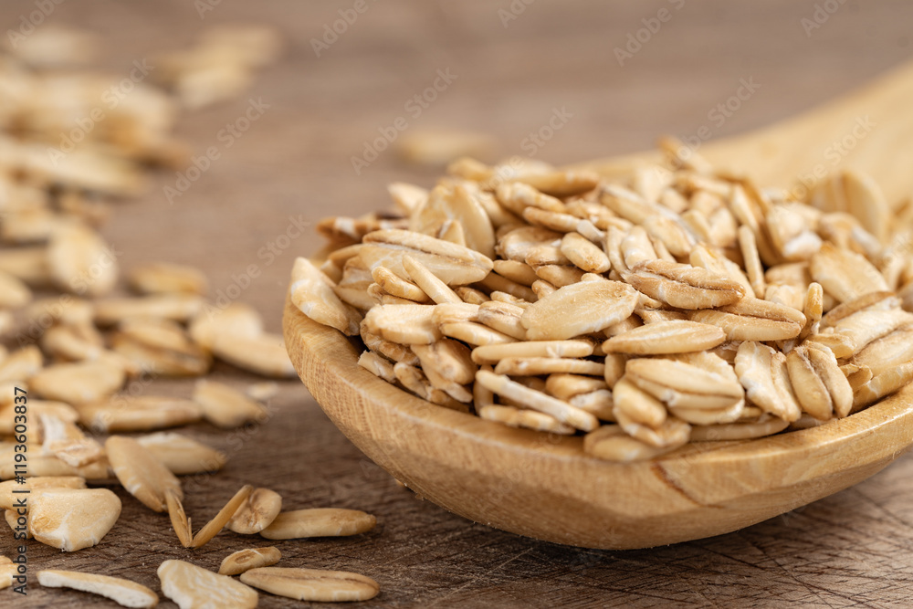 Obraz premium Close-up of raw rolled oats in a wooden spoon on a rustic wooden surface, perfect for healthy eating, natural food, and cooking concepts.