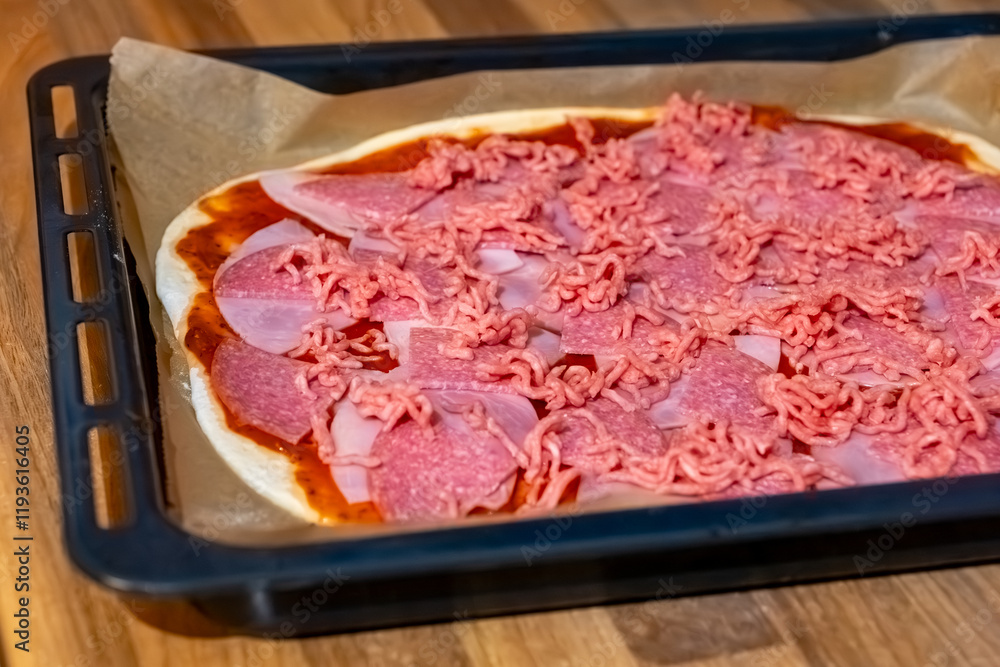 Delicious homemade pizza preparation with various meats and a rich tomato base on a baking tray Delicious homemade pizza preparation with various meats and a rich tomato base on a baking tray