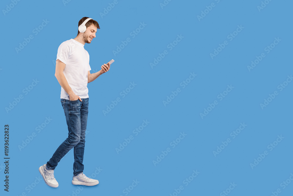 Full length portrait of young man wearing headphones listening to music using cell phone, isolated on purple studio wall Full length portrait of young man wearing headphones listening to music using cell phone, isolated on purple studio wall