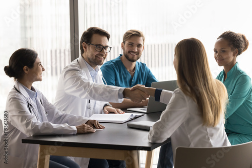 Group of healthcare professionals gathered around table, accomplish team meeting or discussion with handshake, gesture of respect, collaborative, successful teamwork, conclusion of medical concilium