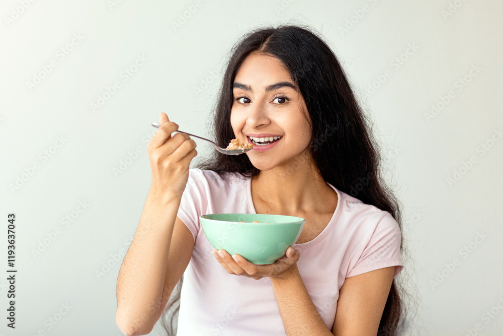Attractive Indian lady having cereal with milk or cornflakes while sitting on comfy bed at home, full length. Lovely Hindu woman having healthy meal, keeping balanced food diet Attractive Indian lady having cereal with milk or cornflakes while sitting on comfy bed at home, full length. Lovely Hindu woman having healthy meal, keeping balanced food diet