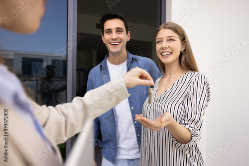 Happy couple buying new house, getting key from realtor, meeting with seller, real estate agent outdoors at apartment entrance. Positive young man and woman renting flat photo