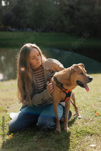 young woman walks with her dog in the park. A lady in a beige raincoat is playing with a pit bull on a green lawn. animal and human friendship, pet training, female dog handler or zoopsychologist photo