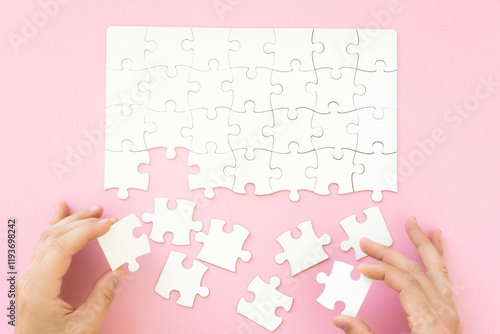 Foto Hands collecting white blank jigsaw puzzle on pink background, top view