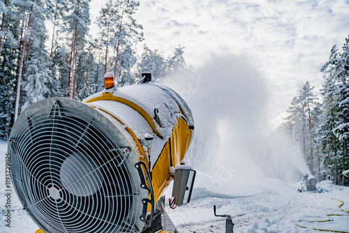 Yellow snow making machine spraying snow in winter using yellow snow canonn to create artificial snow on bright ski resort slope in forest photo