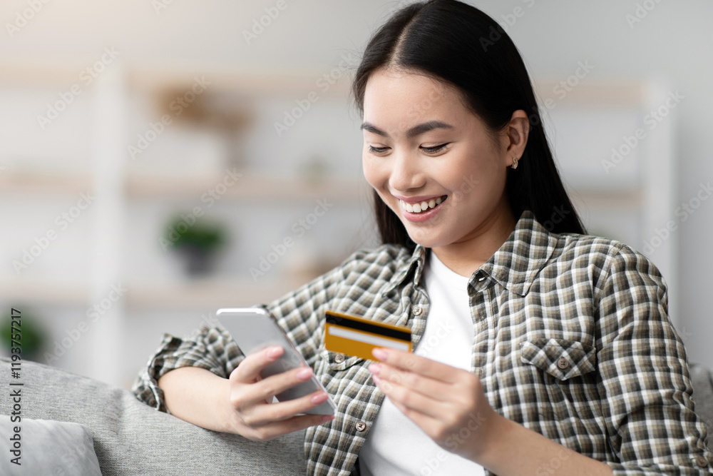 Cheerful young chinese woman holding modern smartphone and credit card, paying for goods and services online while staying home, using mobile application for online shopping, copy space Cheerful young chinese woman holding modern smartphone and credit card, paying for goods and services online while staying home, using mobile application for online shopping, copy space