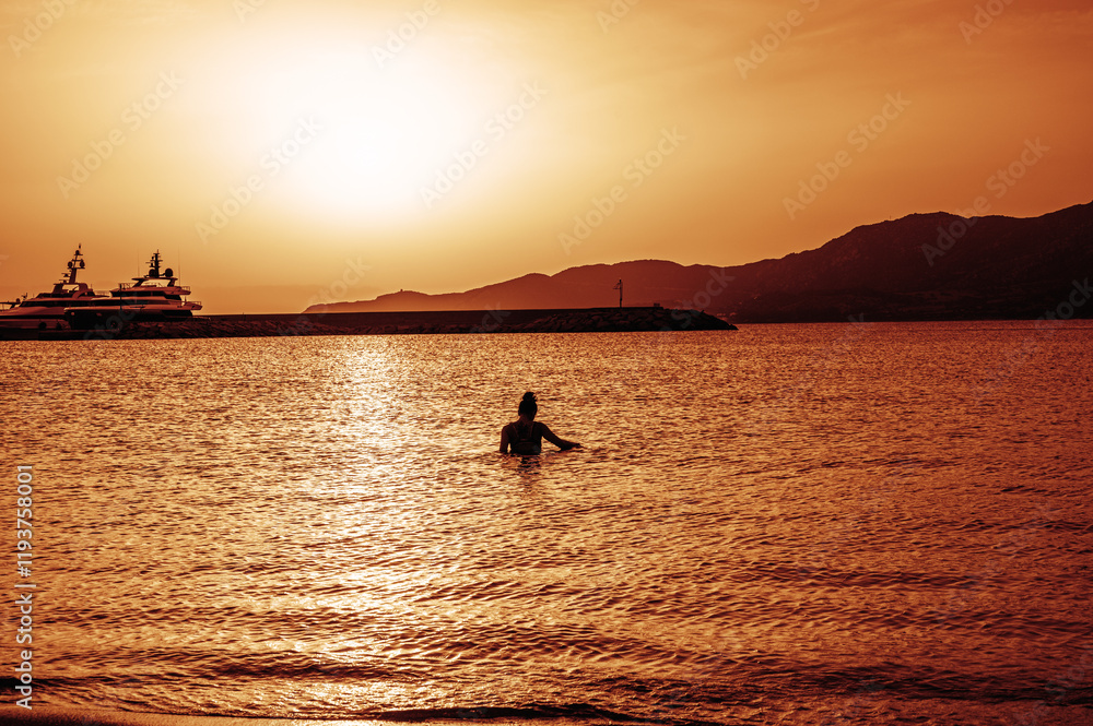 Beautiful sunset with red colors on the sea with a girl in the water turned towards the low sun on the horizon